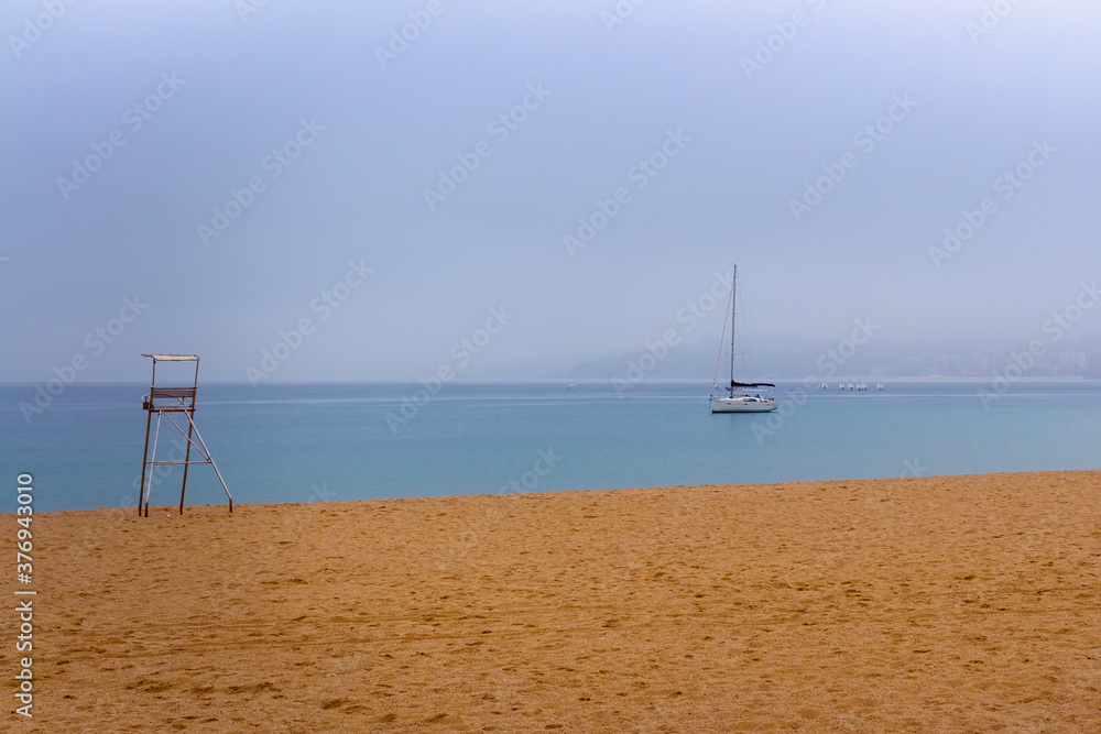 A sailboat anchored among the mist on the beach of the Bahia de Palamos, Costa Brava, Catalonia, Spain A sailboat anchored among the mist on the beach of the Bahia de Palamos, Costa Brava, Catalonia, Spain