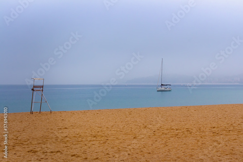 A sailboat anchored among the mist on the beach of the Bahia de Palamos, Costa Brava, Catalonia, Spain