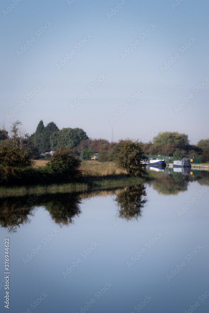 pleasure boats on the canal, calm day with clear reflection on the water, trees and blue sky