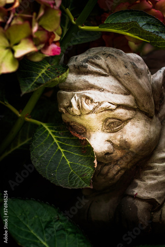 stone garden statue hiding behind leaves with a cheeky smile