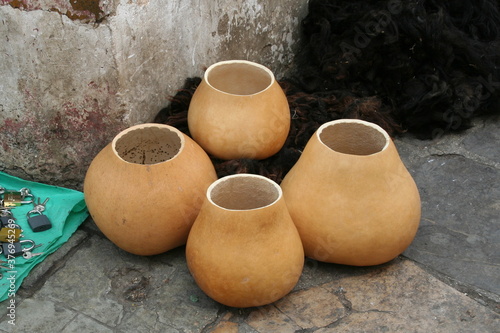 4 duże naczynia z tykw stojące na chodniku przy zniszczonym murze na bazarze w Meksyku obok kłódek i plecionych wełnianych koców