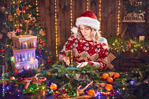 Woman dressed in christmas design sweater making handmade christmas wreath on table for holiday. Christmas decoration and composition.