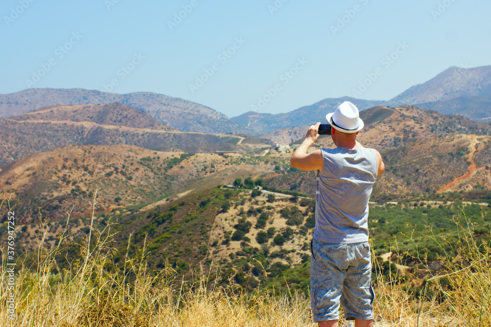 A young man in a hat in the mountains taking pictures of the landscape on a mobile phone