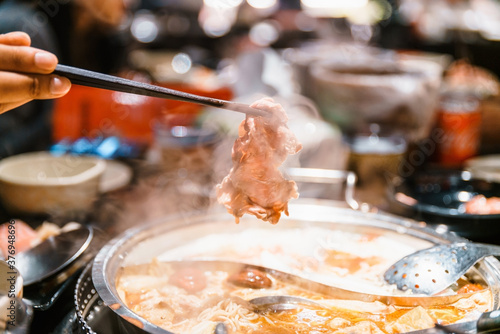 фотографія Hand pinching boiled medium rare slice Wagyu A5 beef out from hot pot Mala soup base by chopsticks