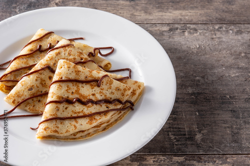 Sweet crepes with chocolate on wooden table.	Copy space