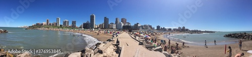 Mar del Plata. Beaches and broken road with people under the blue sky on a sunny day in front of the urban horizon.