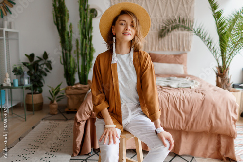 Graceful happy woman in straw hat posing over bohemian interior background. Straw hat , linen  closes. Natural make up.