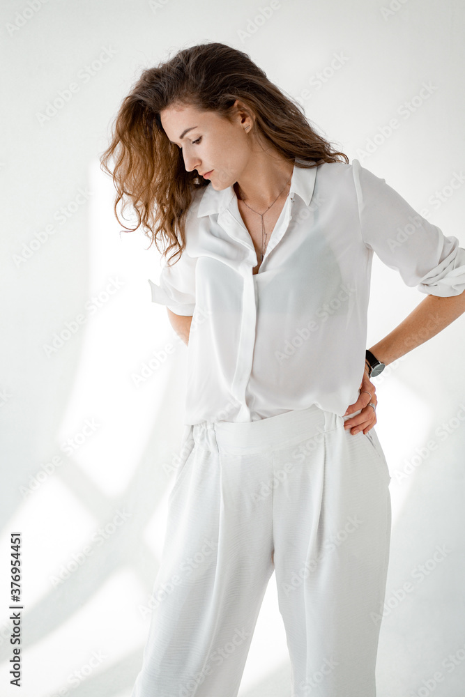 © matyuschenko - Young woman in white shirt on white background. Attractive girl in white clothes on a white background. Studio shot.