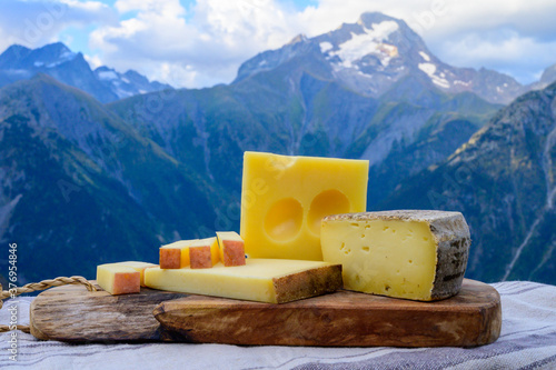 Cheese collection, French beaufort, abondance, emmental, tomme de savoie cheeses served outdoor in Savoy region, with Alpine mountains peaks on background photo