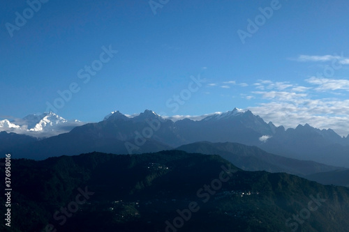 The mighty Kanchanjunga with other snow peaks at the background of a small village on the slope of mountains on the Himalaya from the balcony of a tourist cottage in Sikkim