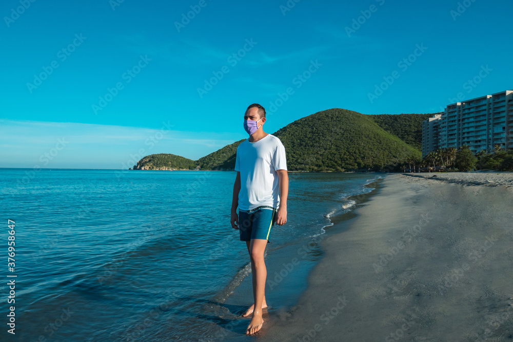 Man with medical mask walking on beach during coronavirus COVID-19 pandemic Man with medical mask walking on beach during coronavirus COVID-19 pandemic