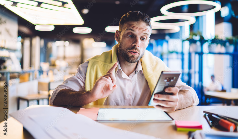 Businessman looking excited while reading message in phone while sitting in cafe