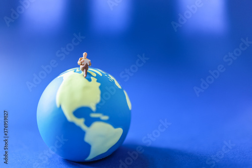 Global Business and Information Concept. Old businessman miniature figure people sitting and reading book or news paper on mini world ball on blue backgrund.
