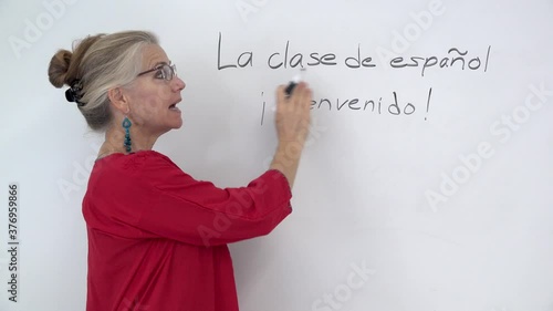 Closeup of pretty woman teaching spanish writing on a whiteboard and smiling and talking to the camera.