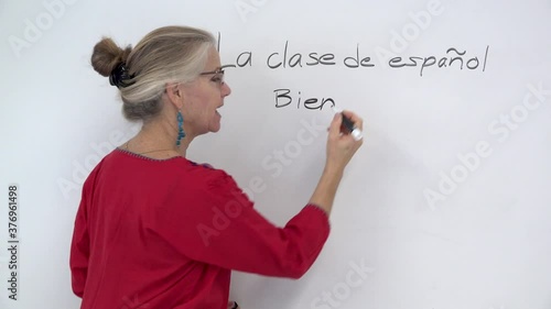 Closeup of pretty woman teaching spanish writing on a whiteboard and smiling and talking to the camera. photo