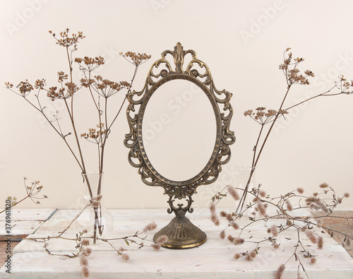 Dried grasses and vintage frame on white wooden table. Composition of dried flowers with empty metal frame indoor.