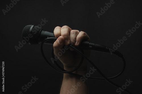 mano sosteniendo micrófono color negro con fondo color negro liso