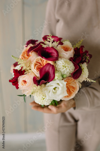 Very nice young woman holding beautiful fresh blossoming bouquet in purple colours of 
Burgundy feces, dahlias, peony roses of David Austin Juliet, white eustoma, burgundy antirinum, astilbe, scabiosa