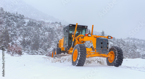 The bulldozer cleans snow on the road, with snowstorm in the background