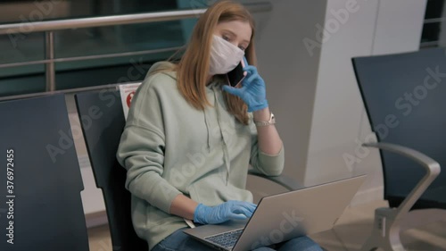 Tired woman in protective mask sitting in a waiting room at the airport and talking on phone, then closing a laptop cover. Real angry axhausted emotions after phone call photo