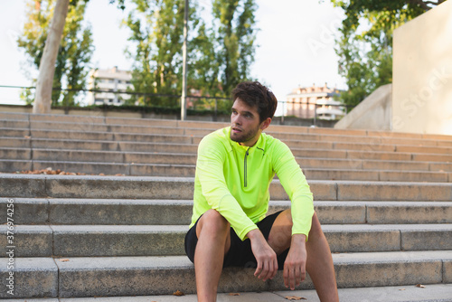 Young bearded man in yellow sportswear is sitting resting after jogging. Lifestyle.