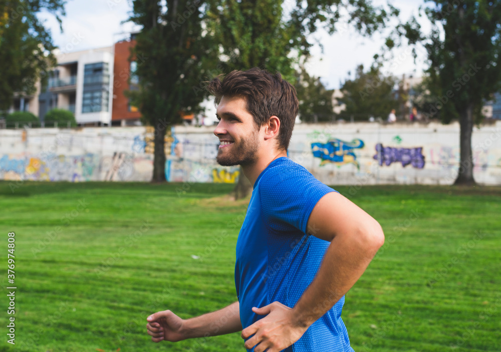 Bearded man dressed in sportswear smiles as he runs through the park. Bearded man dressed in sportswear smiles as he runs through the park.