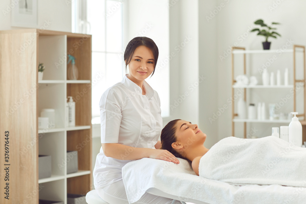 Smiling woman dermatologist sitting near relaxing woman client and preparing for skincare treatment Smiling woman dermatologist sitting near relaxing woman client and preparing for skincare treatment