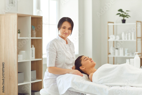 Smiling woman dermatologist sitting near relaxing woman client and preparing for skincare treatment