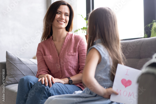 Happy mother's day! Child daughter congratulates mom and gives her postcard. Mum and girl smiling and hugging. Family holiday and togetherness.