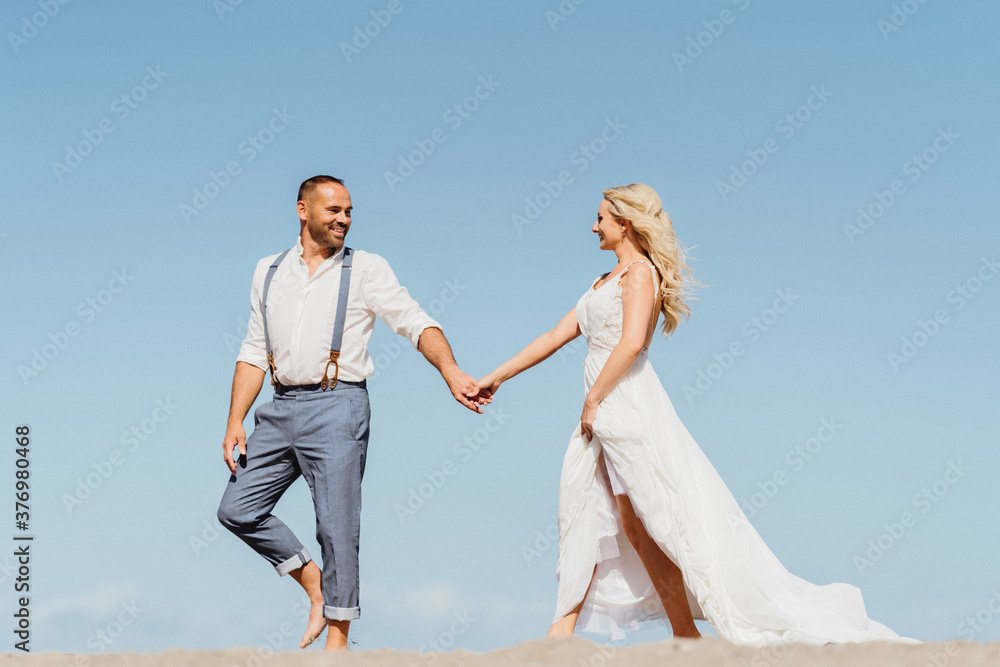 
Happy couple running on the beach holding hands. Beach sand and blue sky with free copy space