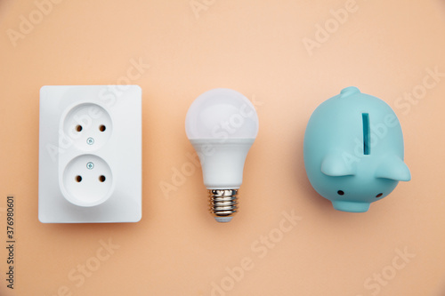 LED light bulb, power socket and blue piggy bank. Power energy economy concept.