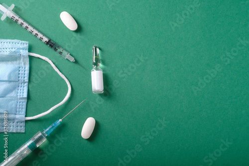 Syringe and ampoule with medicine, pills, place for an inscription, on a green background, top view