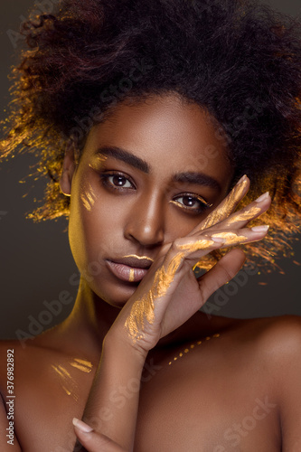 Beautiful african woman with natural make-up with gold sparkles on her face and body. Ethnic makeup. Fashion and Style photo