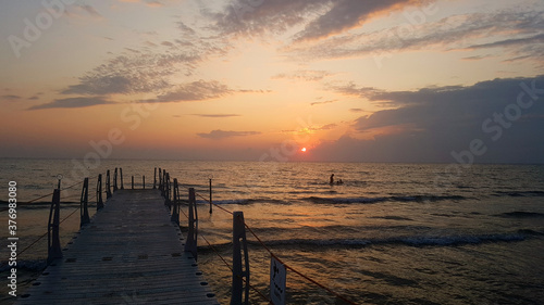 Small sea pier at sunset. Pink sunset in the clouds, small sea waves on a warm summer evening.