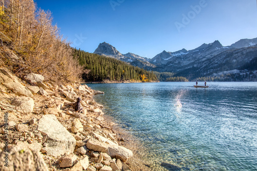 Little boy skipping rocks at lake while 2 men go fishing photo