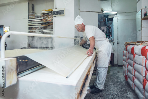 Man Rolling and Steaming Dough at a Bakery in Belgrade, Serbia photo