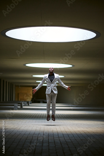 African-American businessman lit by a skylight jumping