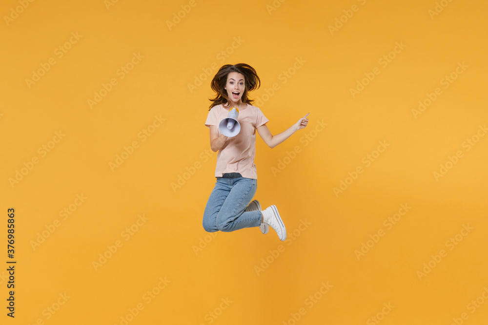 Full length portrait of excited young woman 20s in pastel pink casual t-shirt posing jumping screaming in megaphone pointing index finger aside up isolated on bright yellow color background studio. Full length portrait of excited young woman 20s in pastel pink casual t-shirt posing jumping screaming in megaphone pointing index finger aside up isolated on bright yellow color background studio.