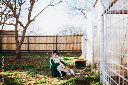 Young boy sitting outside backyard greehouse hugging corgi dog photo