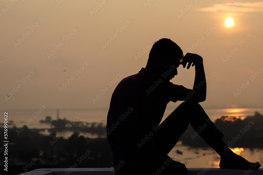 silhouette of a sad man sitting on a pier at sunset