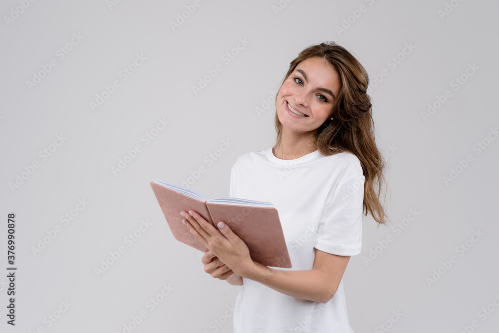 Fototapeta premium Young intelligent excited lady holding notebook in hands isolated on gray background