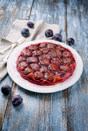 Traditioneller französischer Tarte aux Prunes mit süßen Pflaumen und Vanille angeboten als close-up auf einen Klassic Design Teller mit rustikalen Holz Hintergrund photo