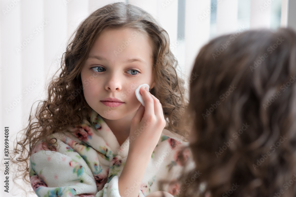 Portrait of beautiful little girl enjoying skincare cleansing procedures front of the mirror in her home bathroom. Portrait of beautiful little girl enjoying skincare cleansing procedures front of the mirror in her home bathroom.