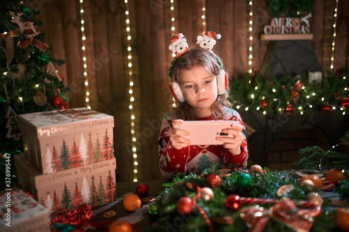 Girl using phone near Christmas tree in the decorative interior. Christmas and New Year photo.