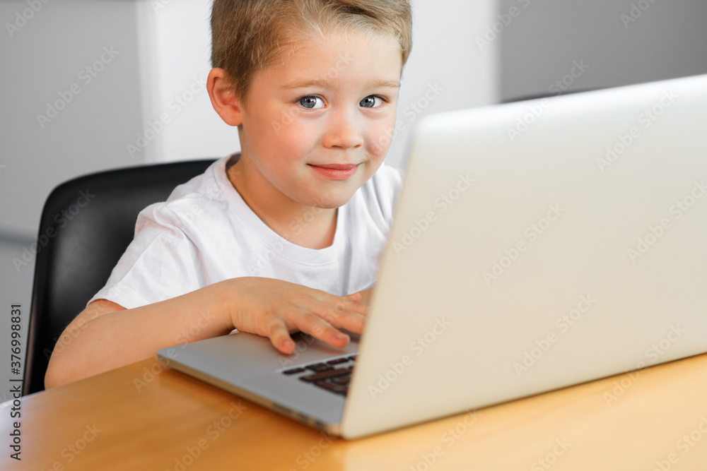 A young boy using a laptop computer sitting on top of a tableundefined at home A young boy using a laptop computer sitting on top of a tableundefined at home