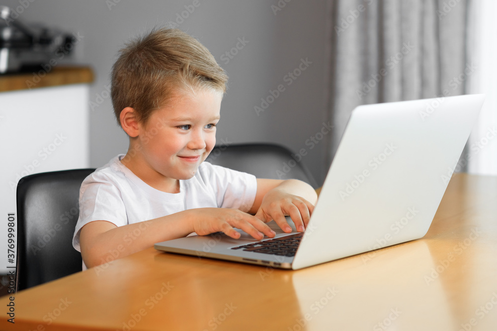 Funny young boy using a laptop computer sitting on top of a tableundefined at home Funny young boy using a laptop computer sitting on top of a tableundefined at home