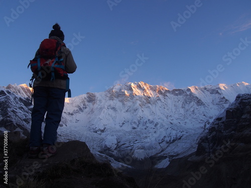 A mountain climber standing on a rock near the top and watches the sunrise over a snow-covered rock, ABC (Annapurna Base Camp) Trek, Annapurna, Nepal