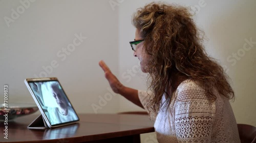 Side shot of a spanish woman making a video call on a tablet with her mother infected with coronavirus COVID 19 while staying at the hospital thanks to the volunteer team that make that calls photo