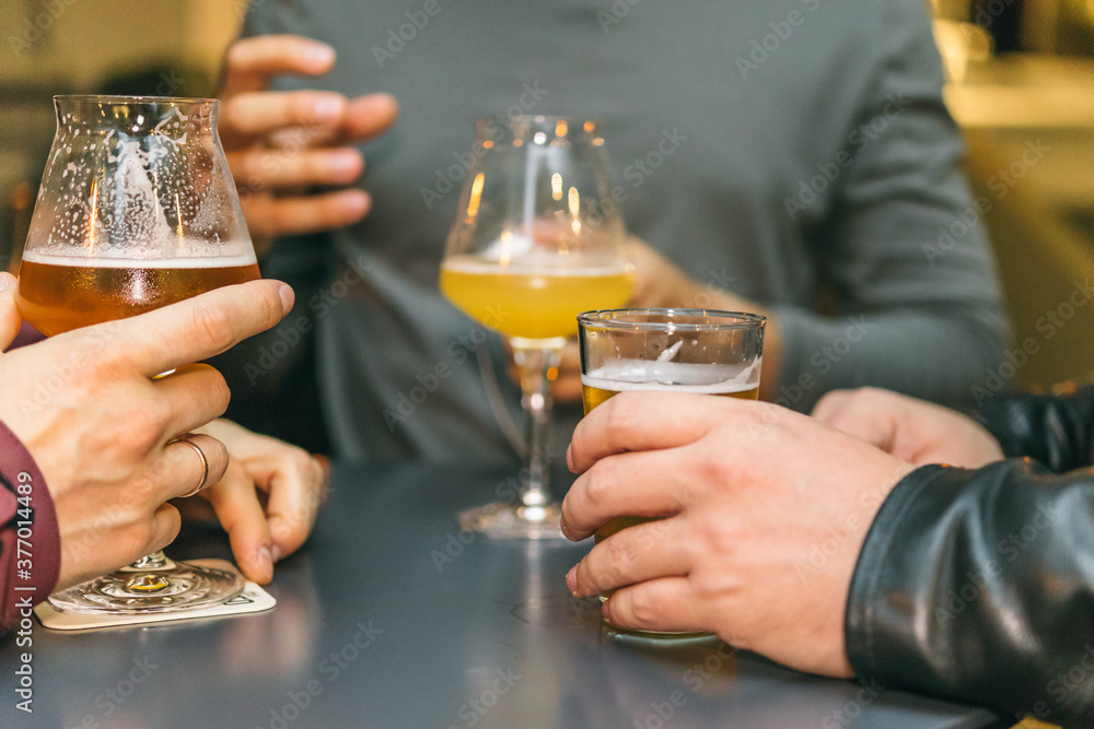 A group of friends at the bar drinking beer at a table. Close-up of male hands and glasses with alcohol