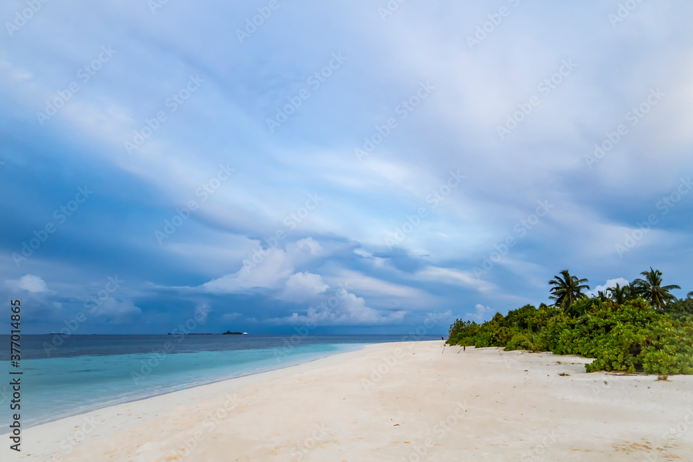Obraz premium Tropical island shore with white sand and forest at sunset against sky with clouds